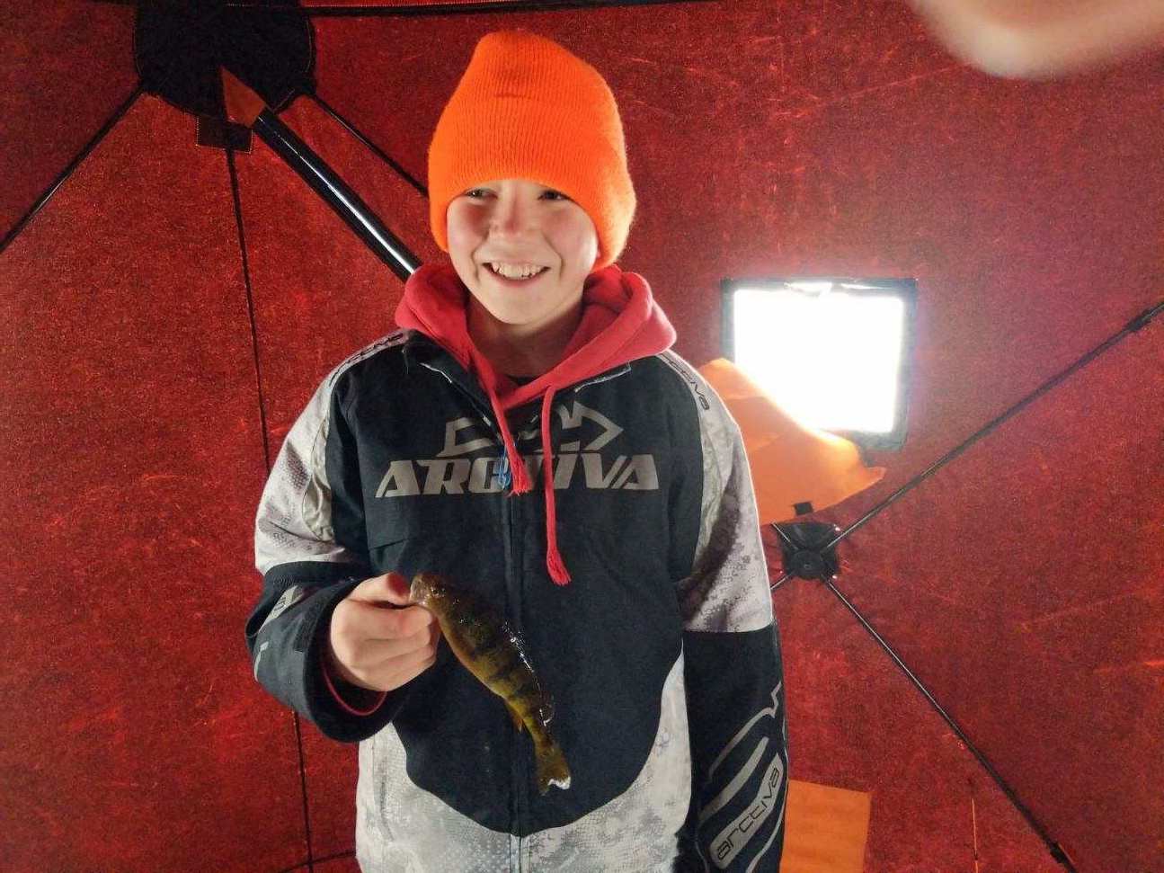 A boy in an orange hat proudly holds a fish he caught, showcasing his fishing skills and enthusiasm.