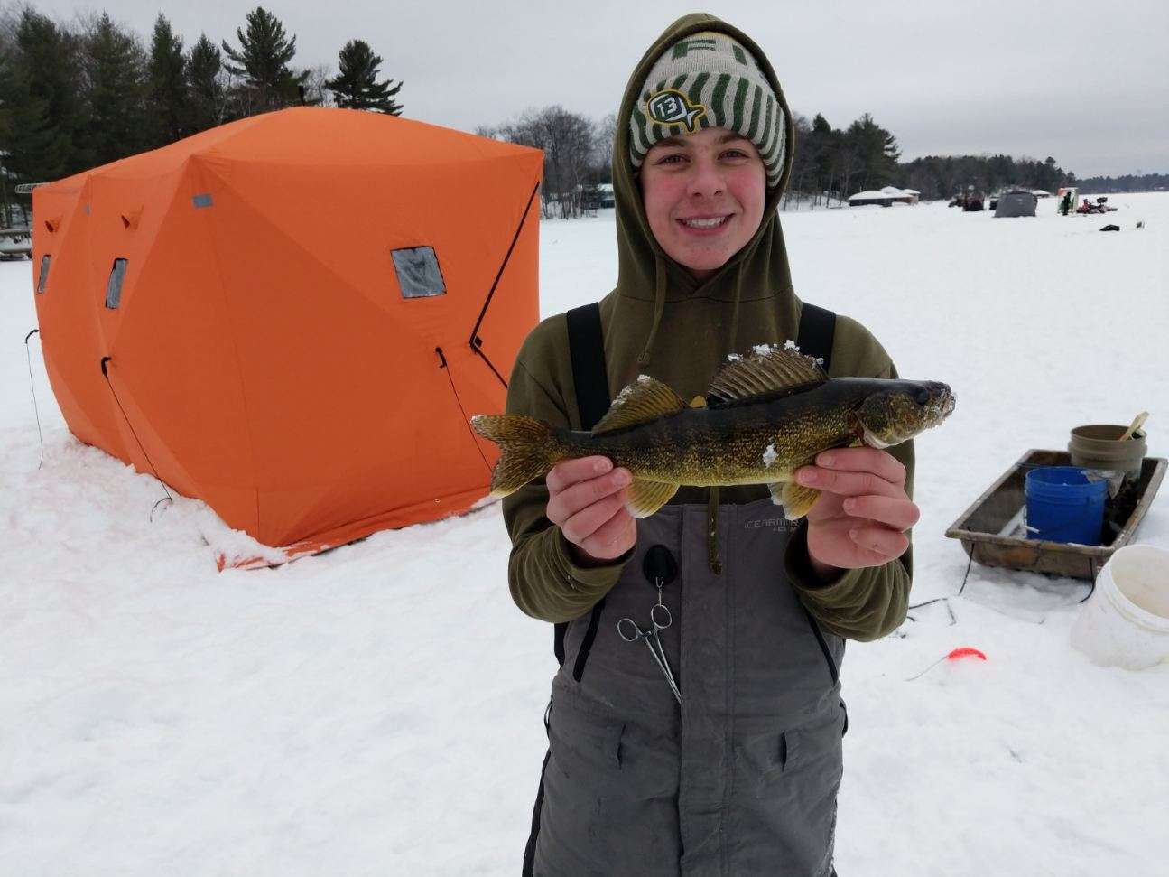 A young man holding a fish in the snow, showcasing his winter fishing success.