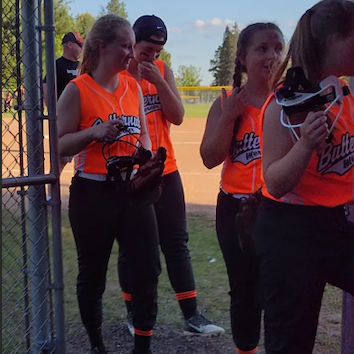 A team of softball players posing in front of a fence, ready for a game.