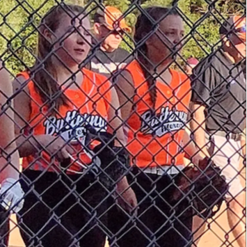 Several girls in orange and black uniforms standing behind a fence.