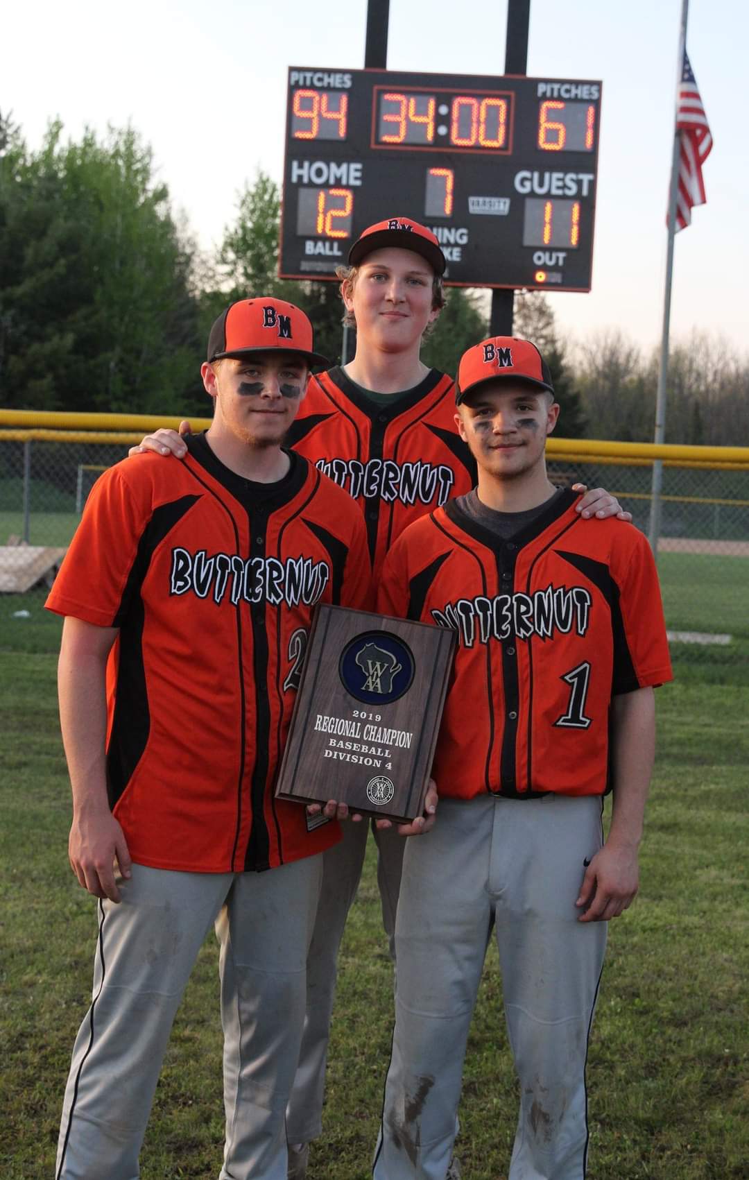 Three baseball players posing with a plaque on the field.