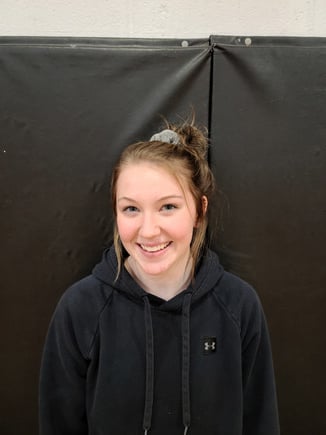 A girl in a black hoodie standing in front of a black wall.