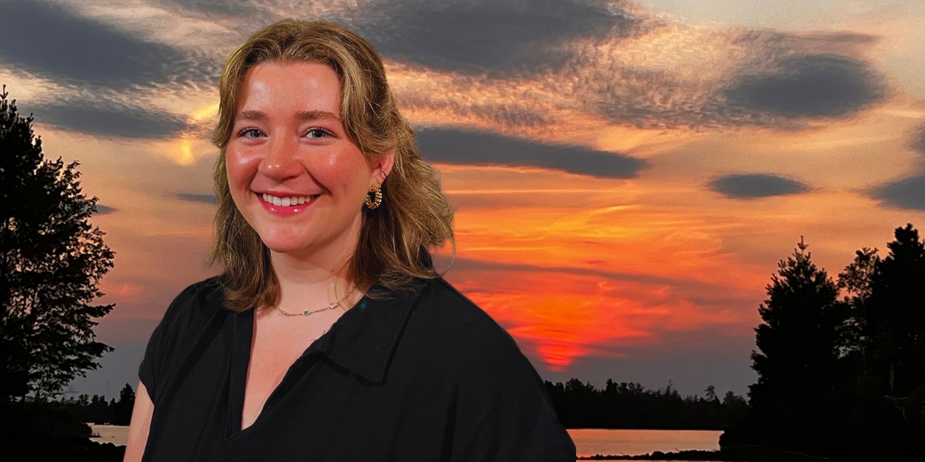 A woman smiling in front of a beautiful sunset, radiating joy and contentment.