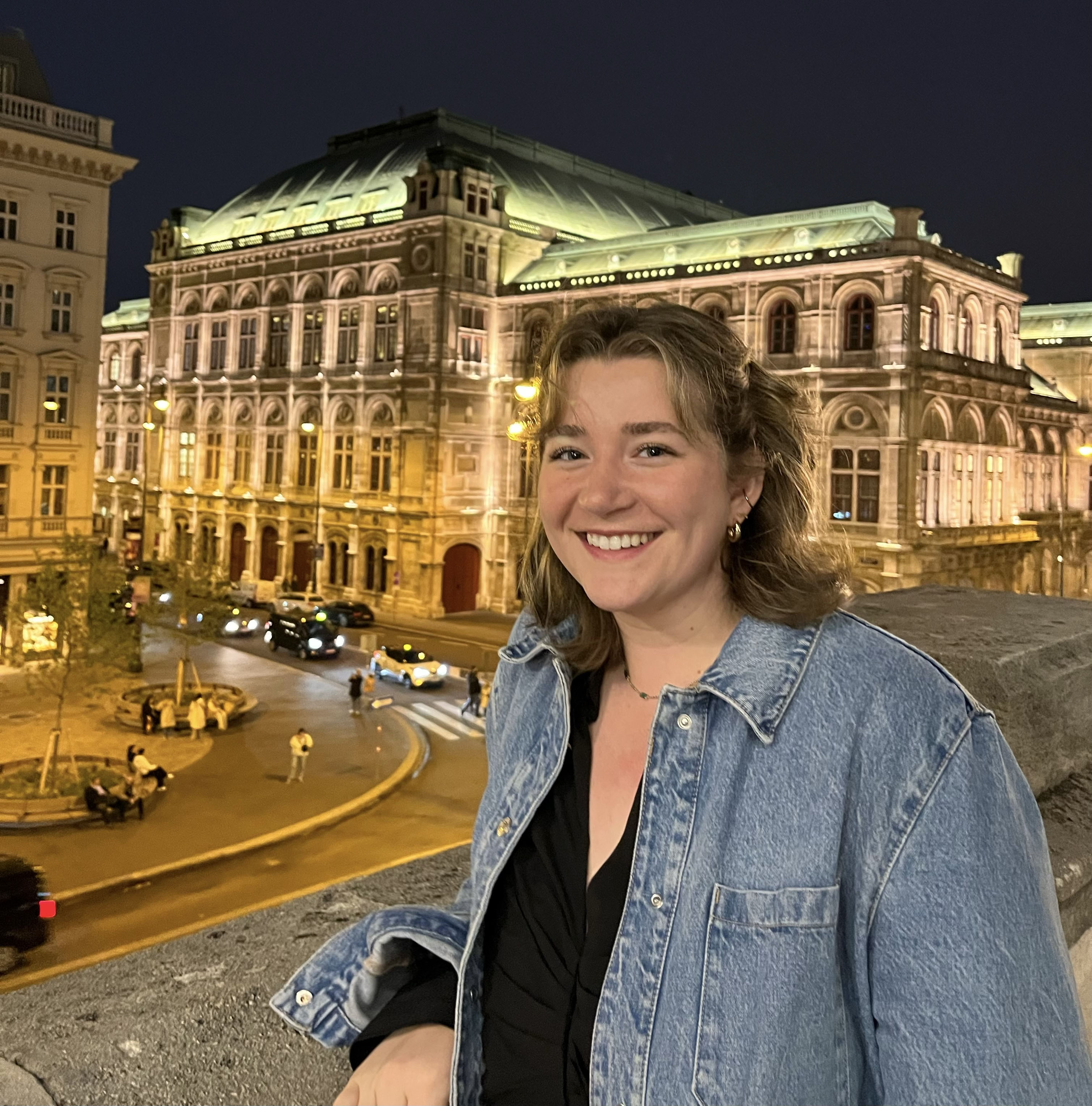 A woman smiling in front of a building at night, radiating joy and contentment in the city's nocturnal ambiance.