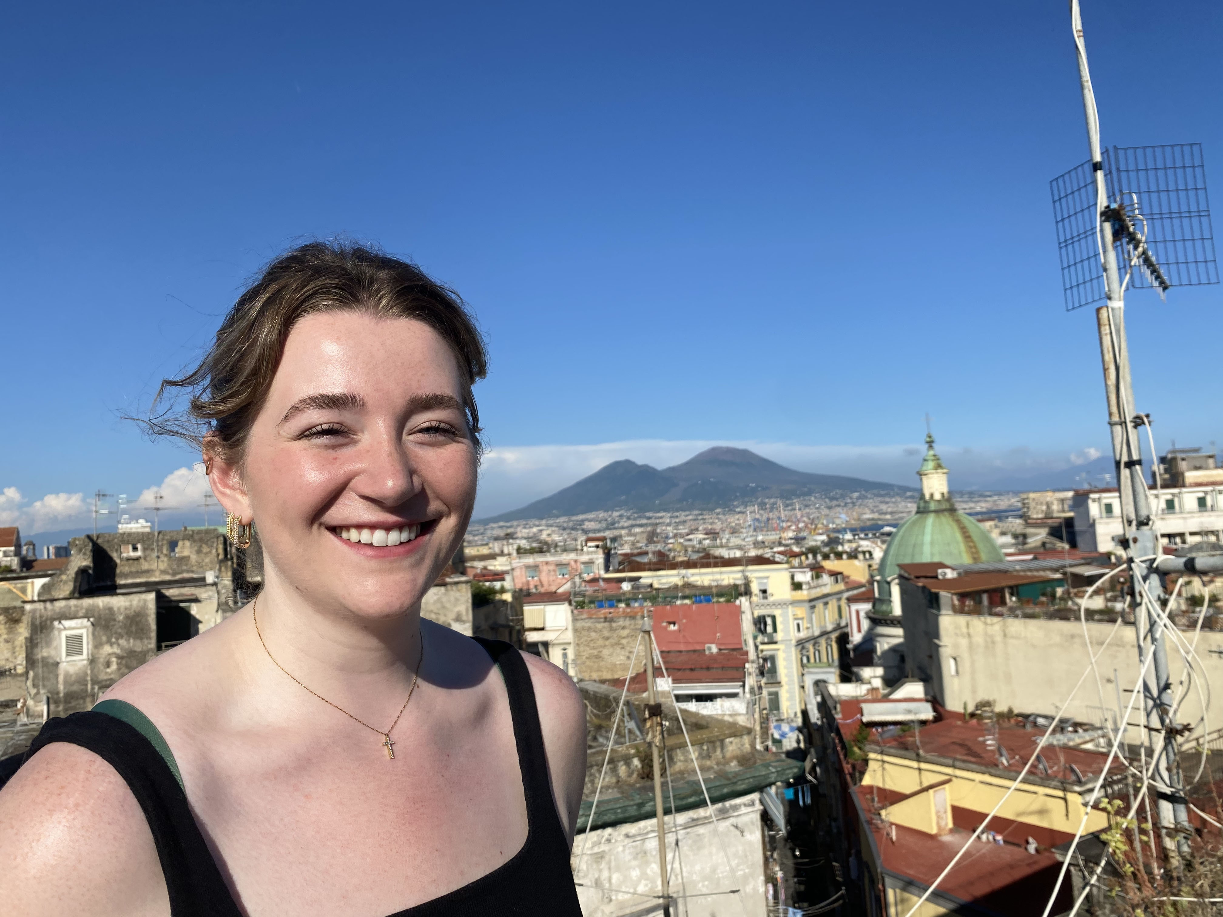 A woman smiling on a rooftop with a city in the background, radiating joy and capturing the urban beauty.