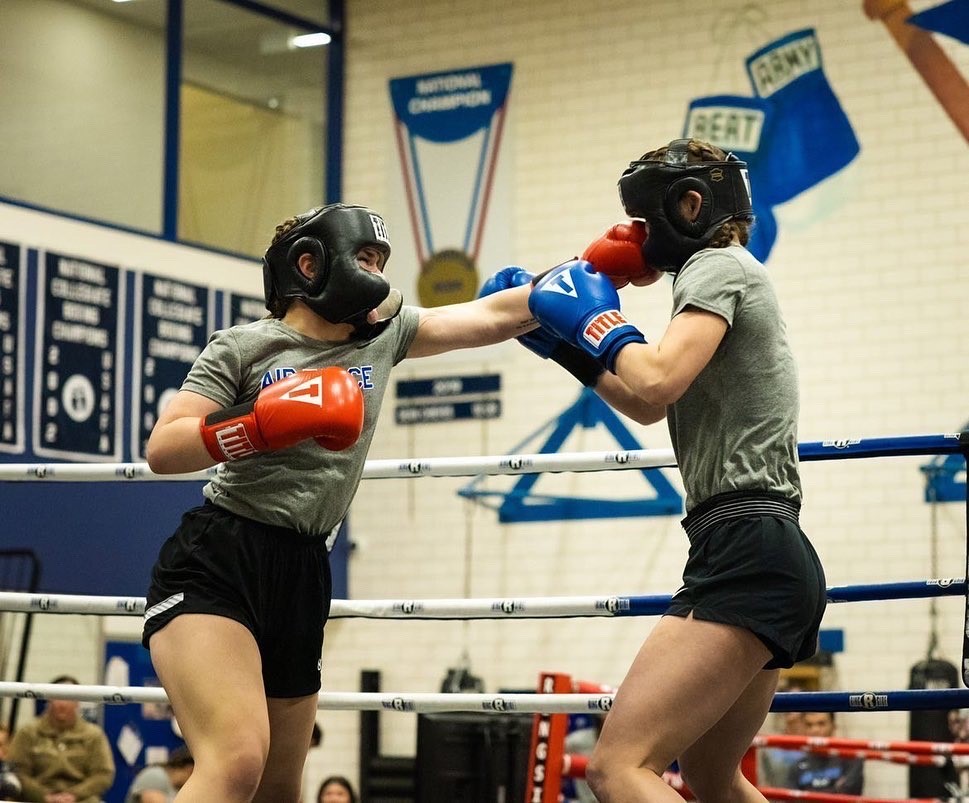 Two women wearing boxing gear, training in a gym.