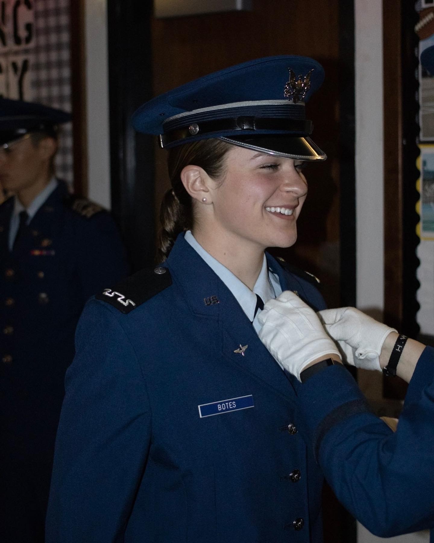 A woman in uniform carefully attaches a badge to her chest.