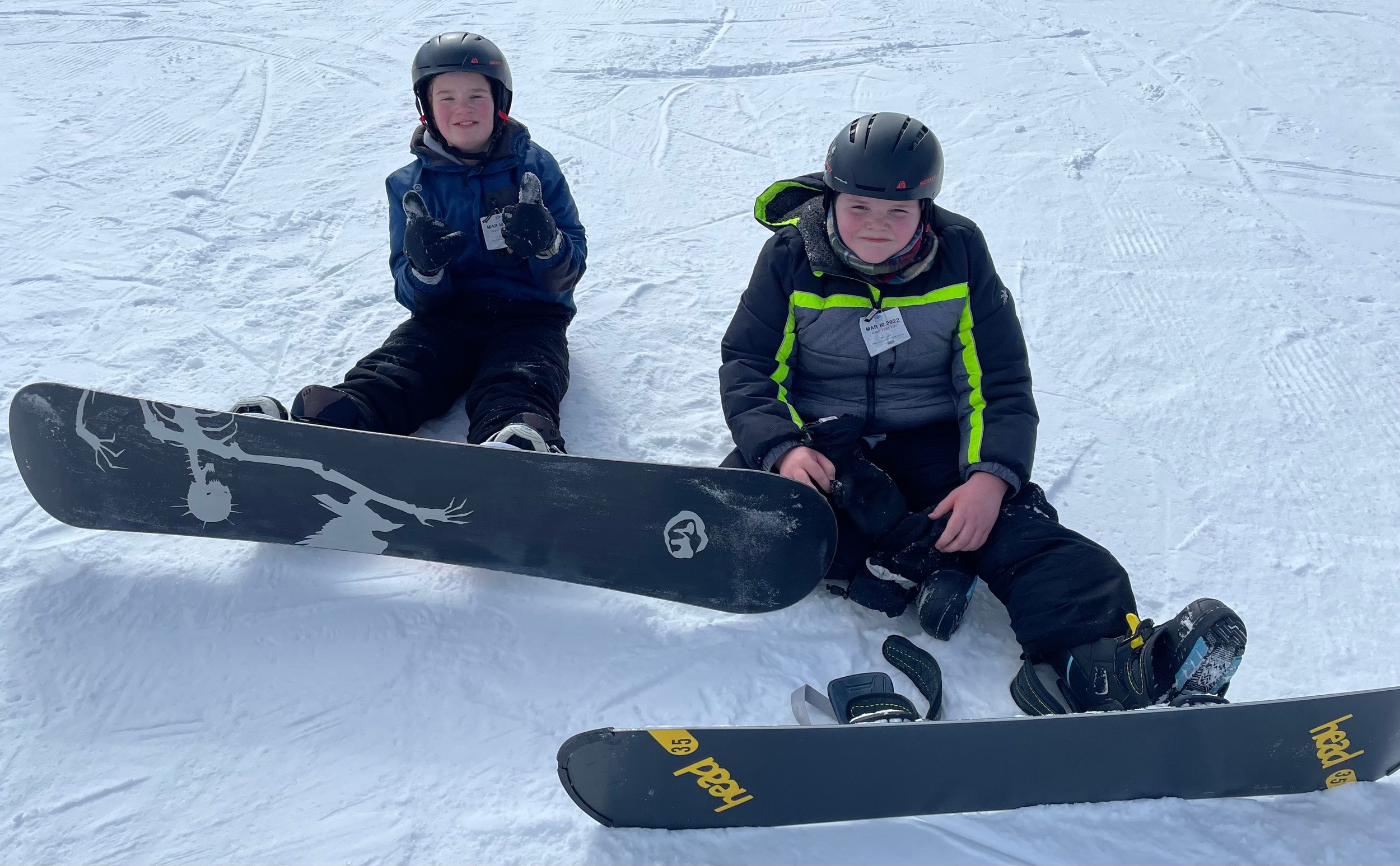 Two young men sitting on snow with snowboards