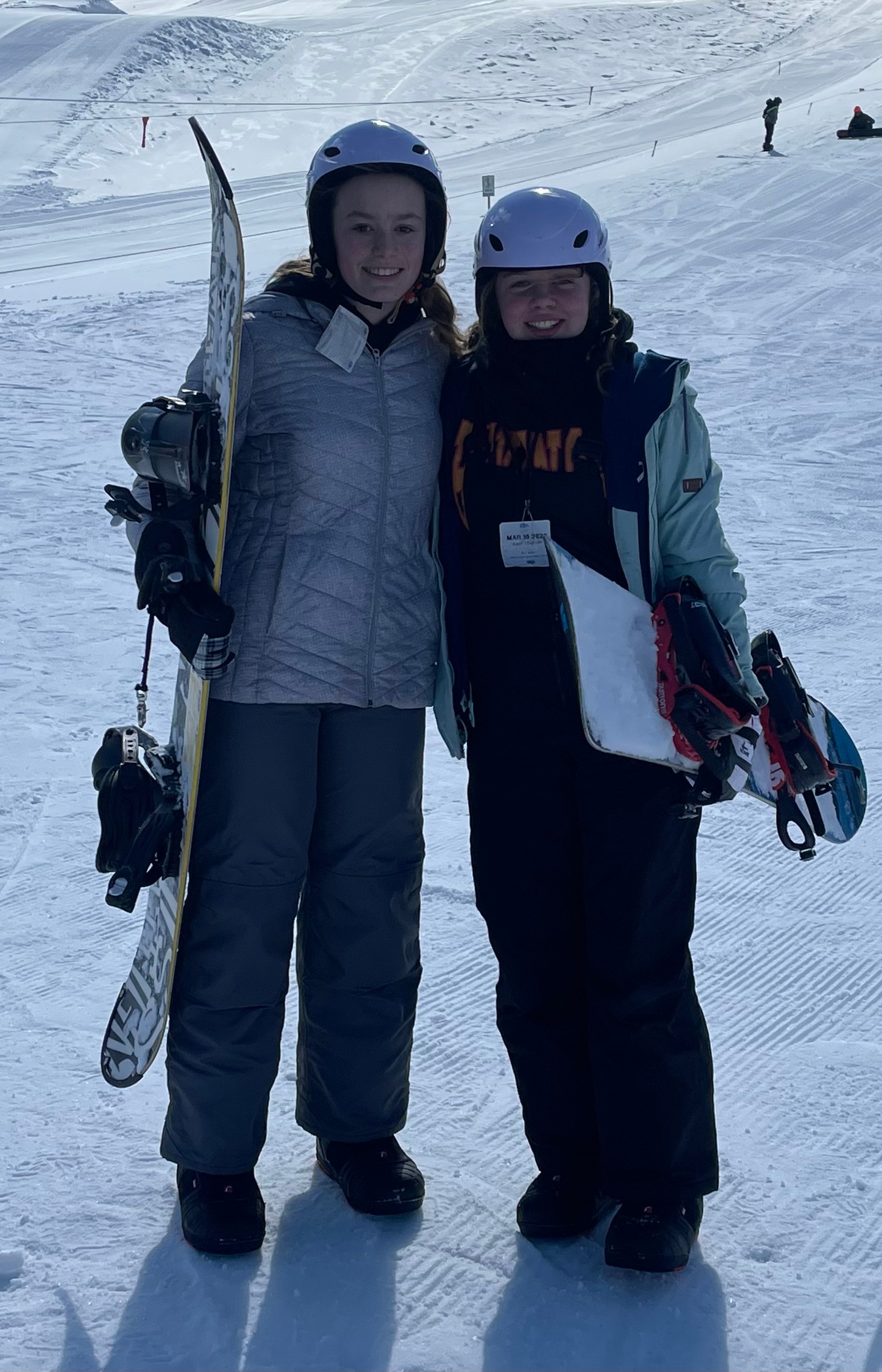 Two young girls smiling and standing on a snow-covered slope