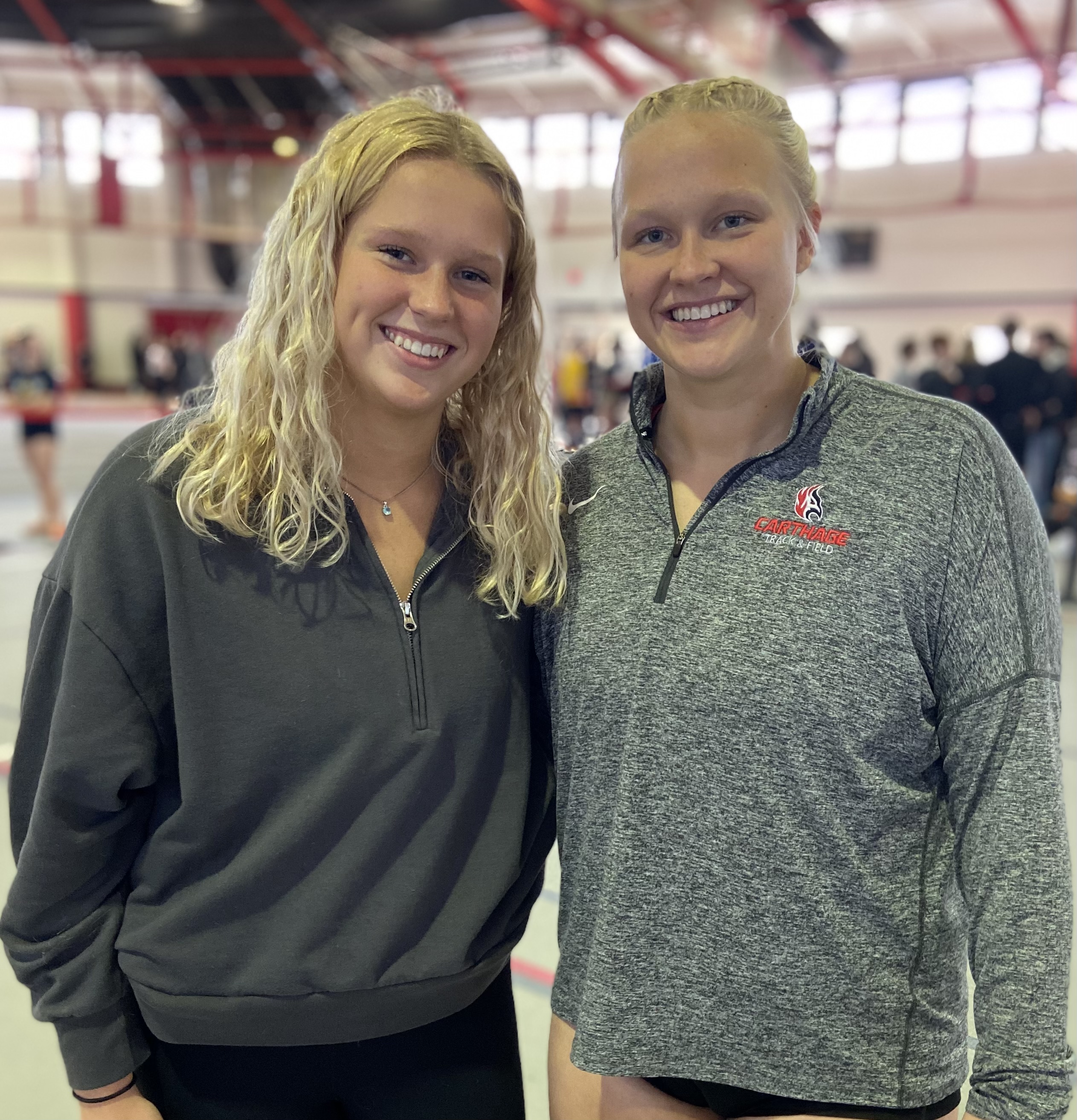 Two women in gym attire standing together, smiling, in a fitness center.