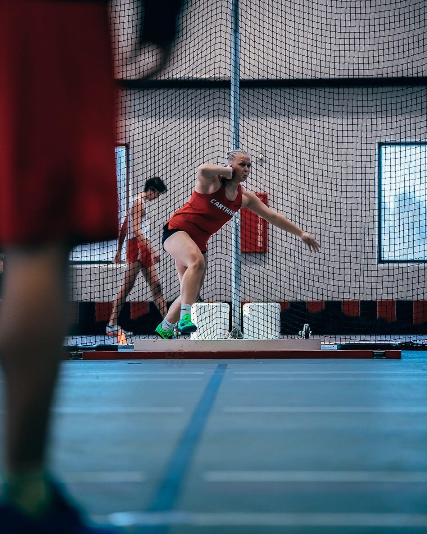 A woman in a red shirt throwing a discus during a sports event.