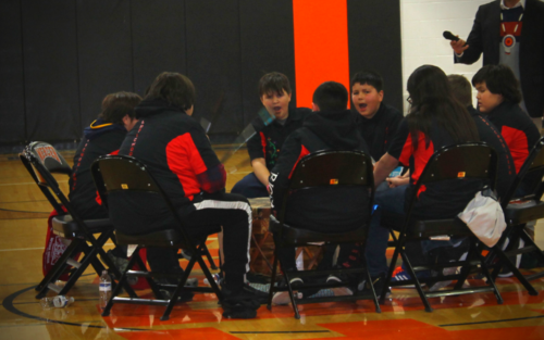 A group of people sitting on chairs in a gym.