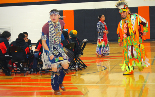 Two men in Native American costumes dancing energetically at a cultural event.