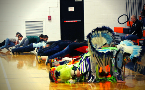 A diverse group of people in traditional attire sitting on the floor.