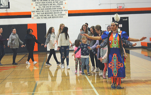 A group of people in traditional clothing dancing joyfully in a gymnasium.