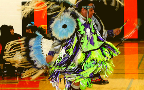 A man in a vibrant costume dancing on a basketball court.