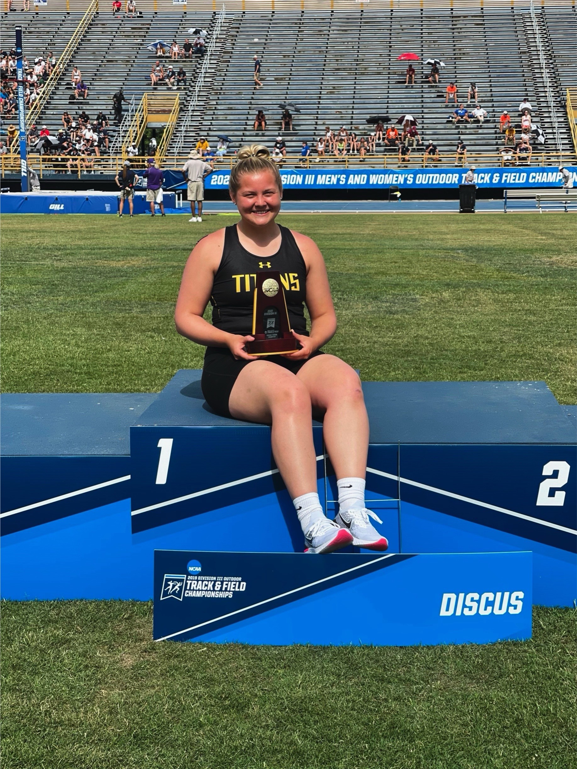 A girl proudly sits on a podium, clutching a trophy in her hands, symbolizing her victory and achievement.