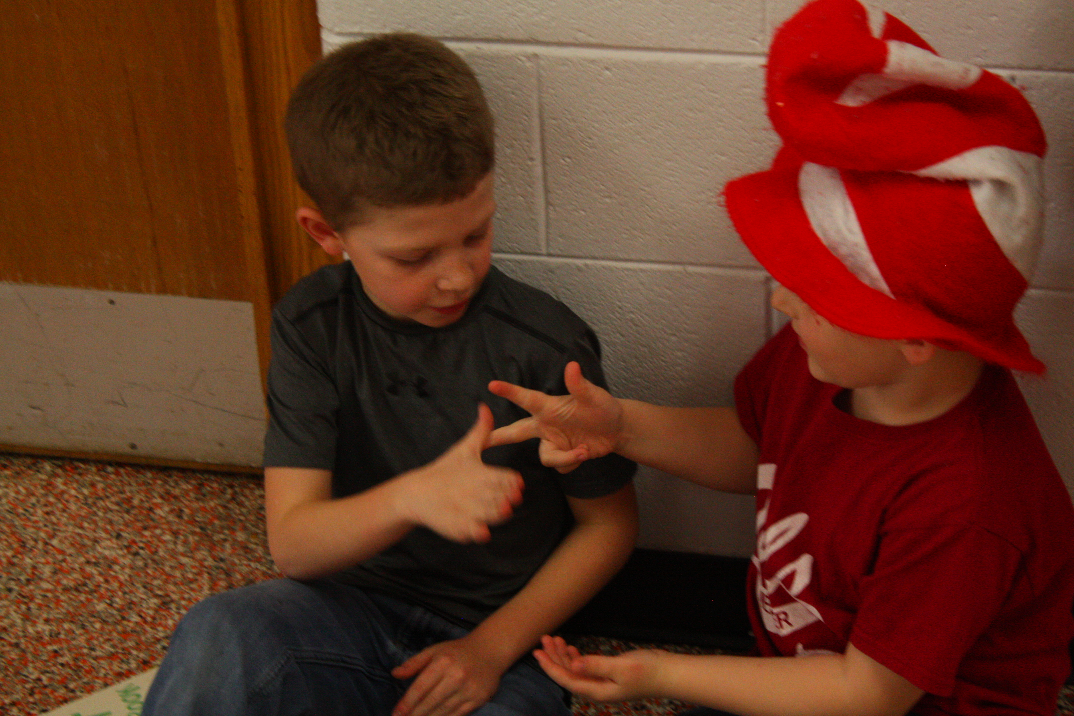 Two boys sitting on the floor with a cat wearing a hat.