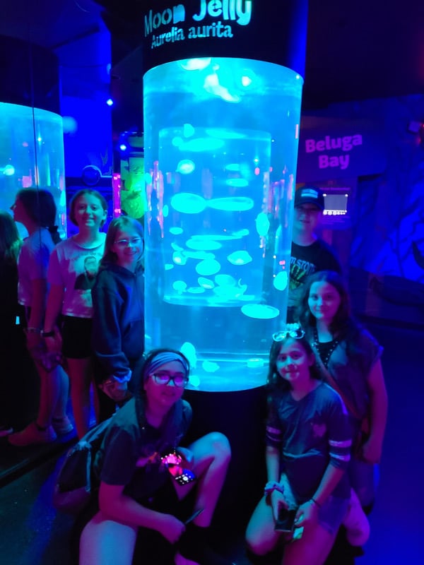 Children smiling in front of a huge aquarium filled with colorful fish.