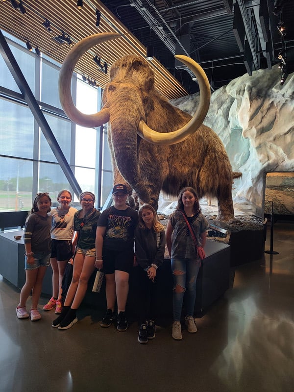 A diverse group of people posing in front of a mammoth