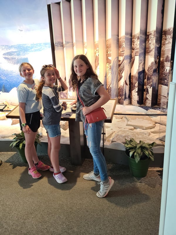 Three girls posing in front of a ship display.