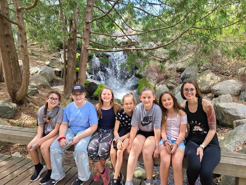 A joyful bunch of kids sitting on a bench, enjoying the mesmerizing view of a waterfall.