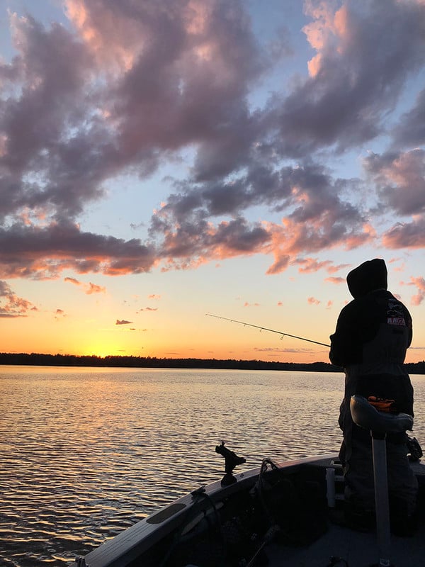  A man on a boat fishing at sunset