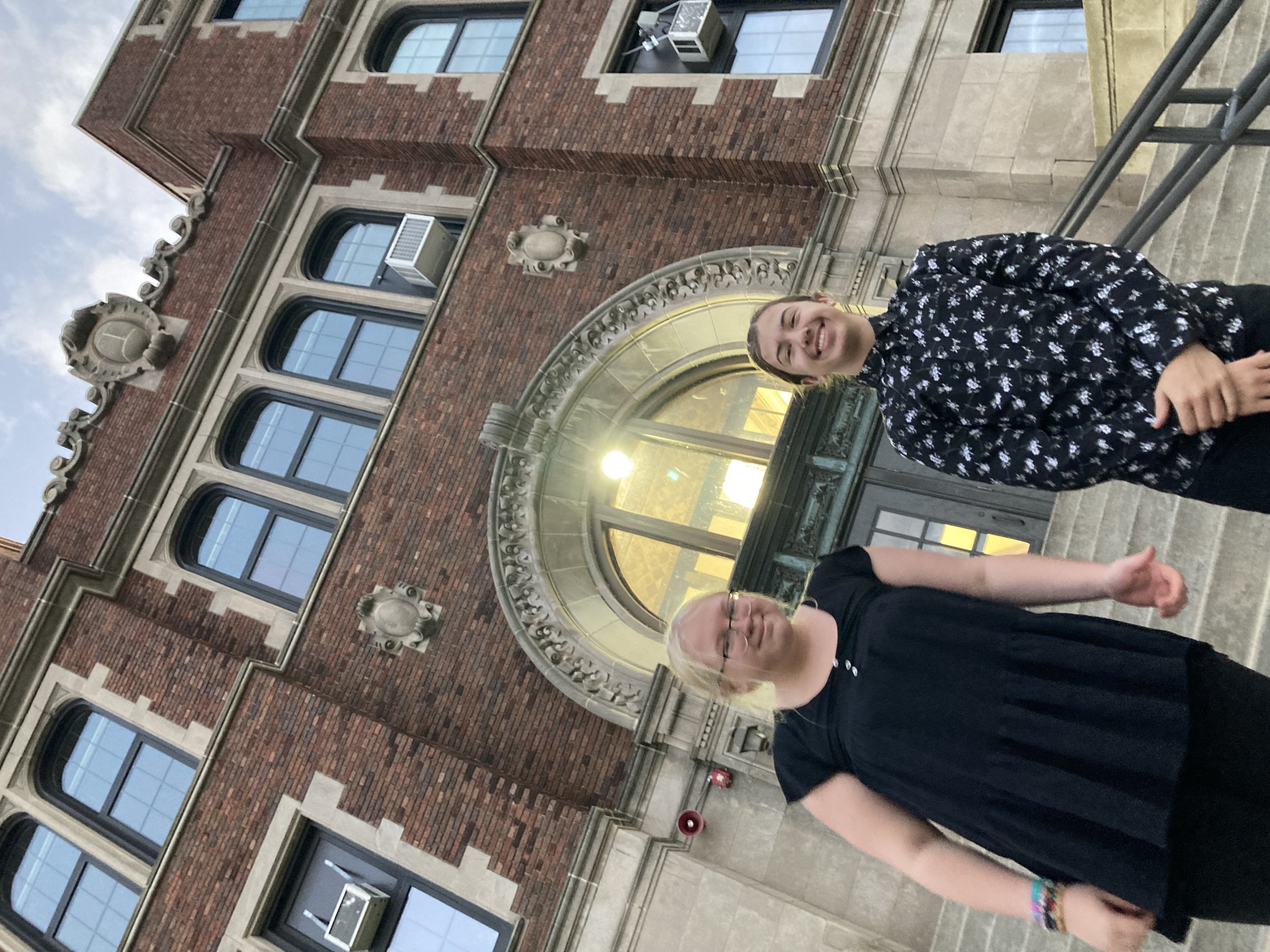 Two peaople standing in front of a building, smiling and looking at the camera.