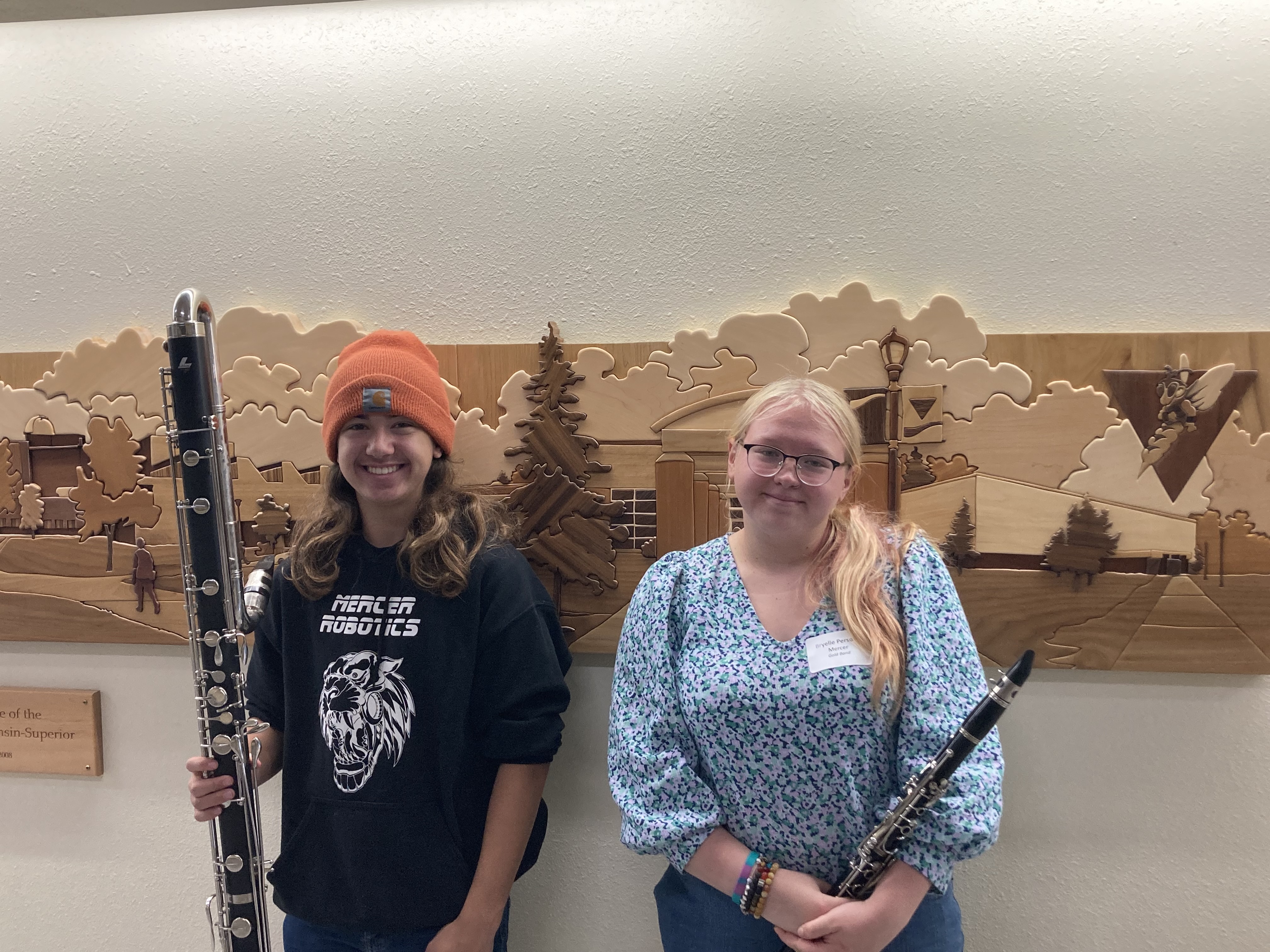 Two young females holding flutes against a wall.