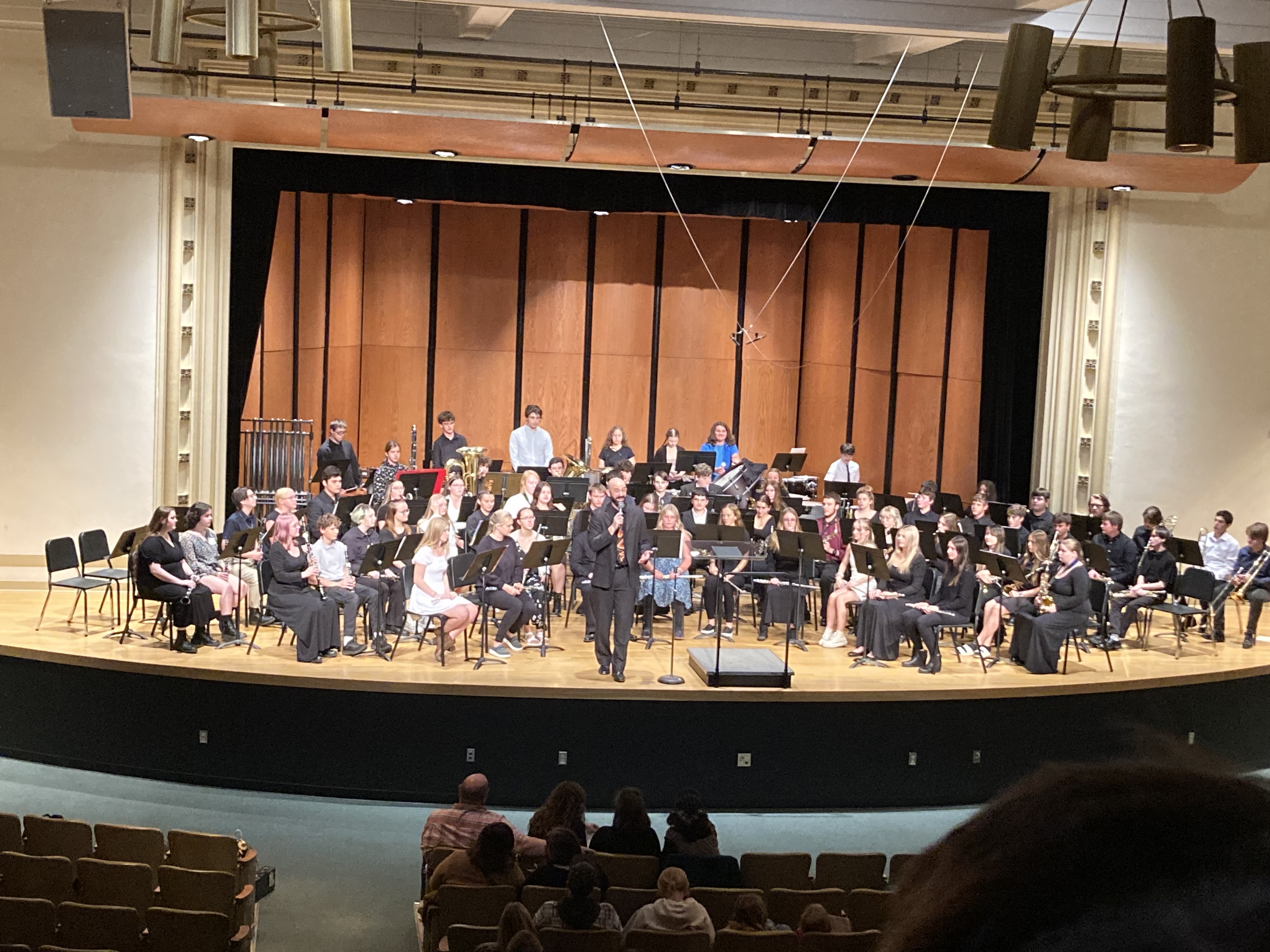 A band performing on stage in a packed auditorium with audience watching attentively.