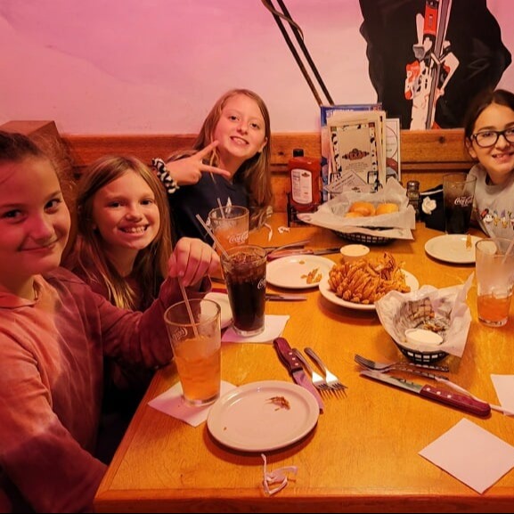 Group of young women sitting around a table, eating and drinking together.