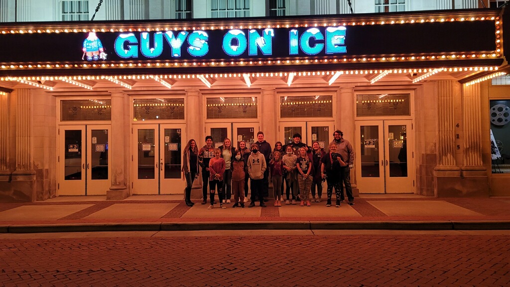 A crowd of people gathered outside a theater with a sign that reads "Guys on Ice".