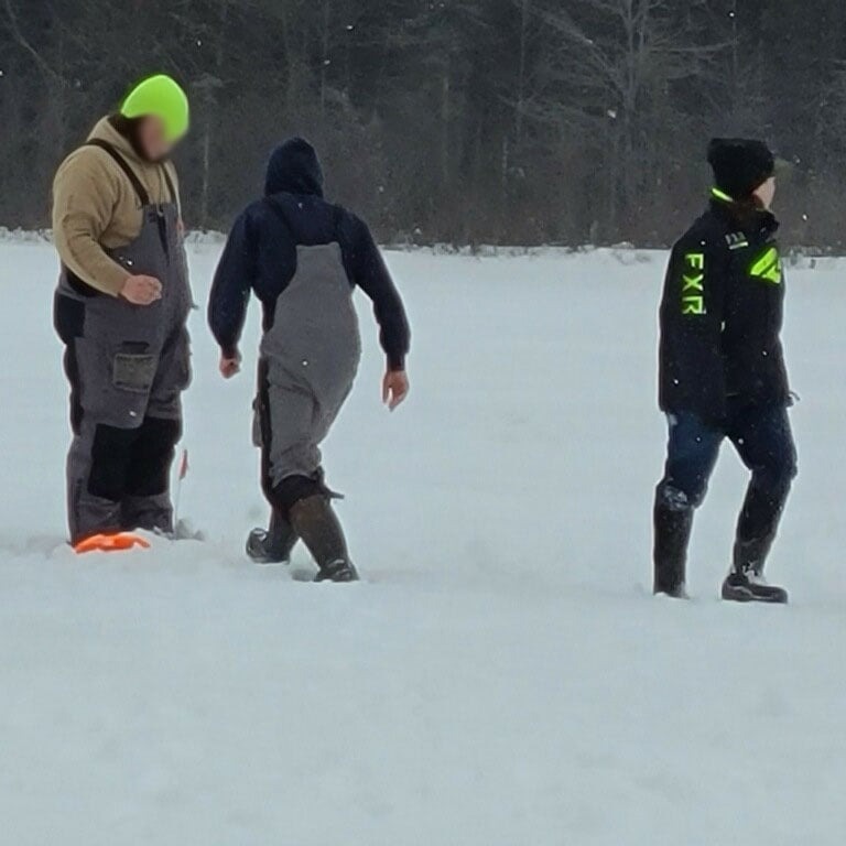 Three people walking across a snow-covered field, with snowflakes falling gently from the sky.