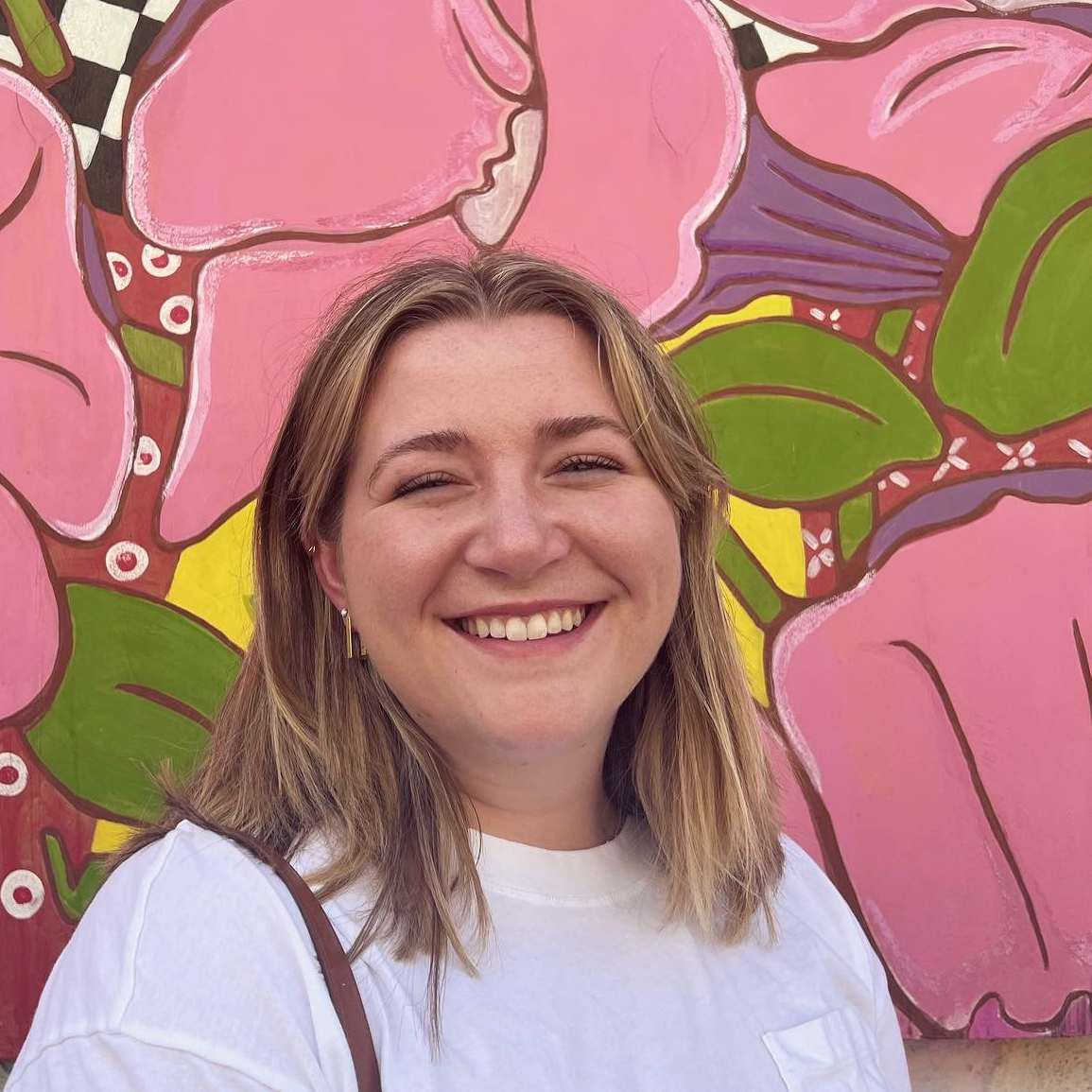 Zoe Botes posing in front of flower paintingpink flowers with green leaves, background pattern varies with checkerboard and dusty rose coler with white circles