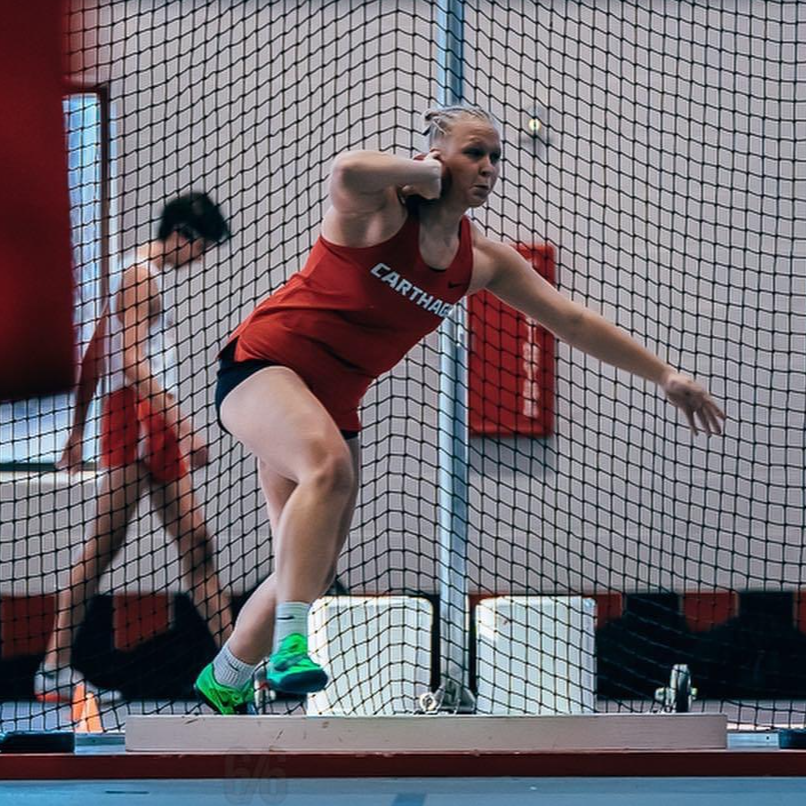 Aubrey throwing shot put in Carthage College track uniform