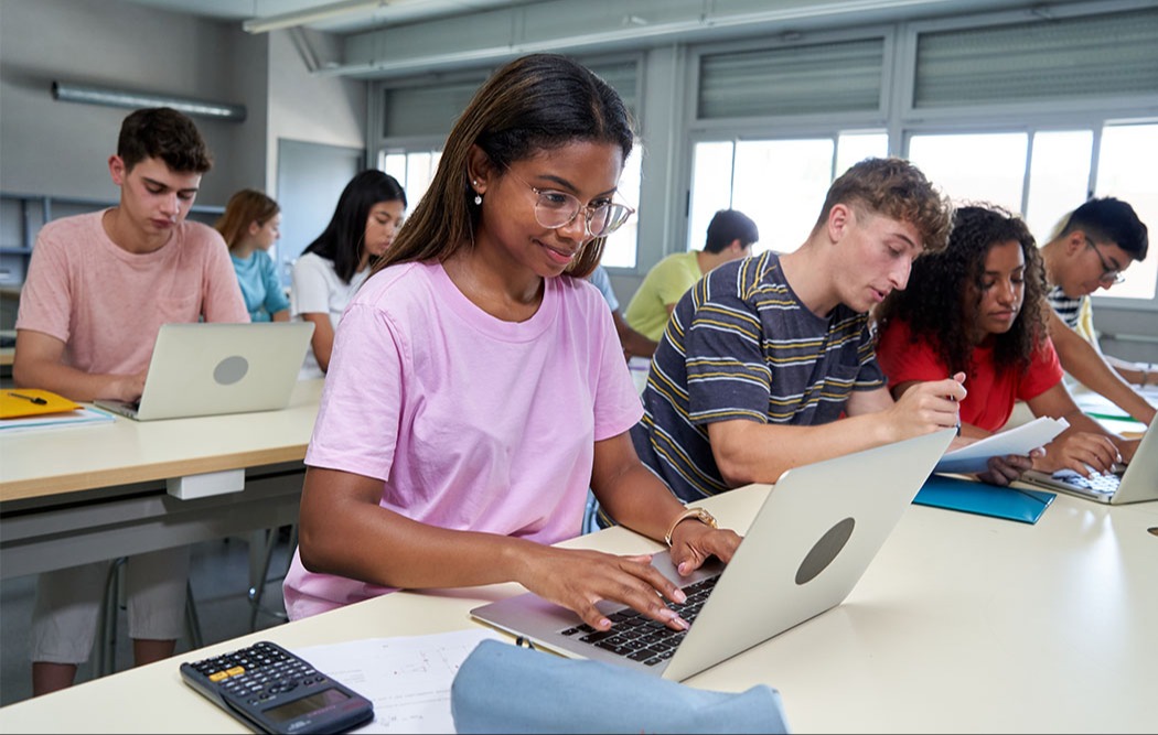 Students working collaboratively in a classroom with laptops and notebooks.