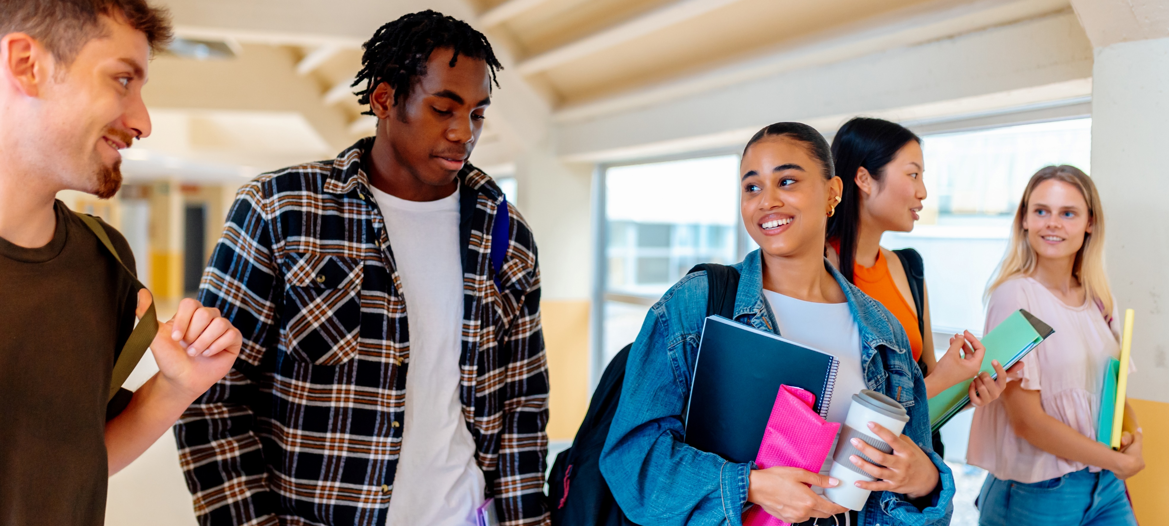 A group of five diverse students walking together in a school hallway, smiling and carrying books and backpacks.