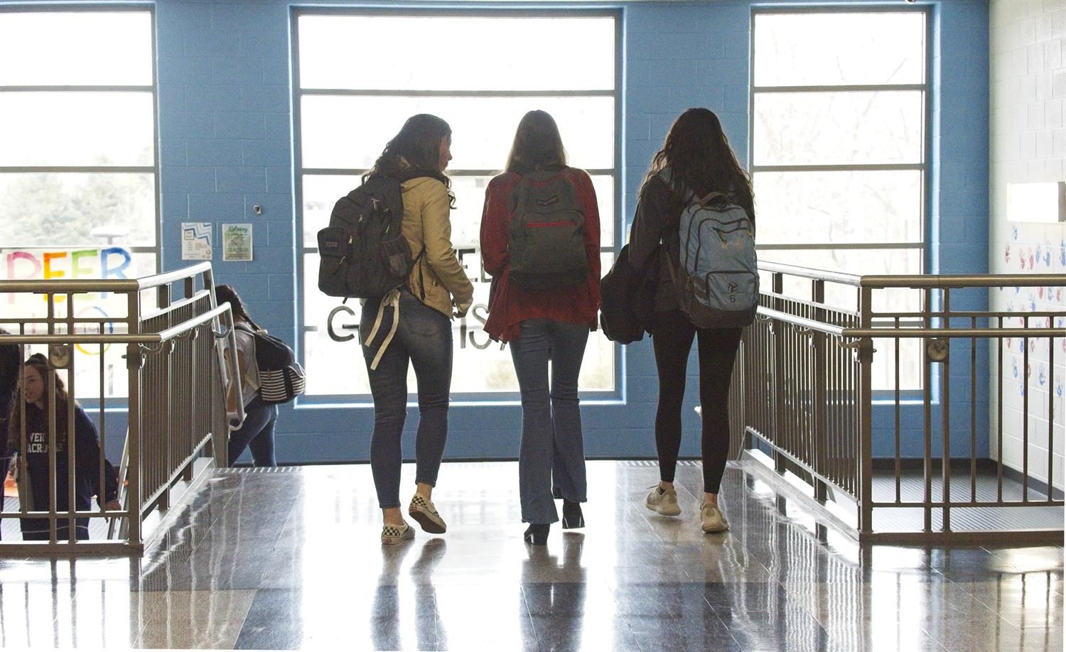 group of 3 female students walking through a hallway, their backs to the camera