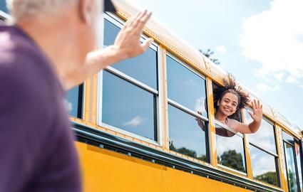 Parent waving to child as they leave on a school bus to attend school