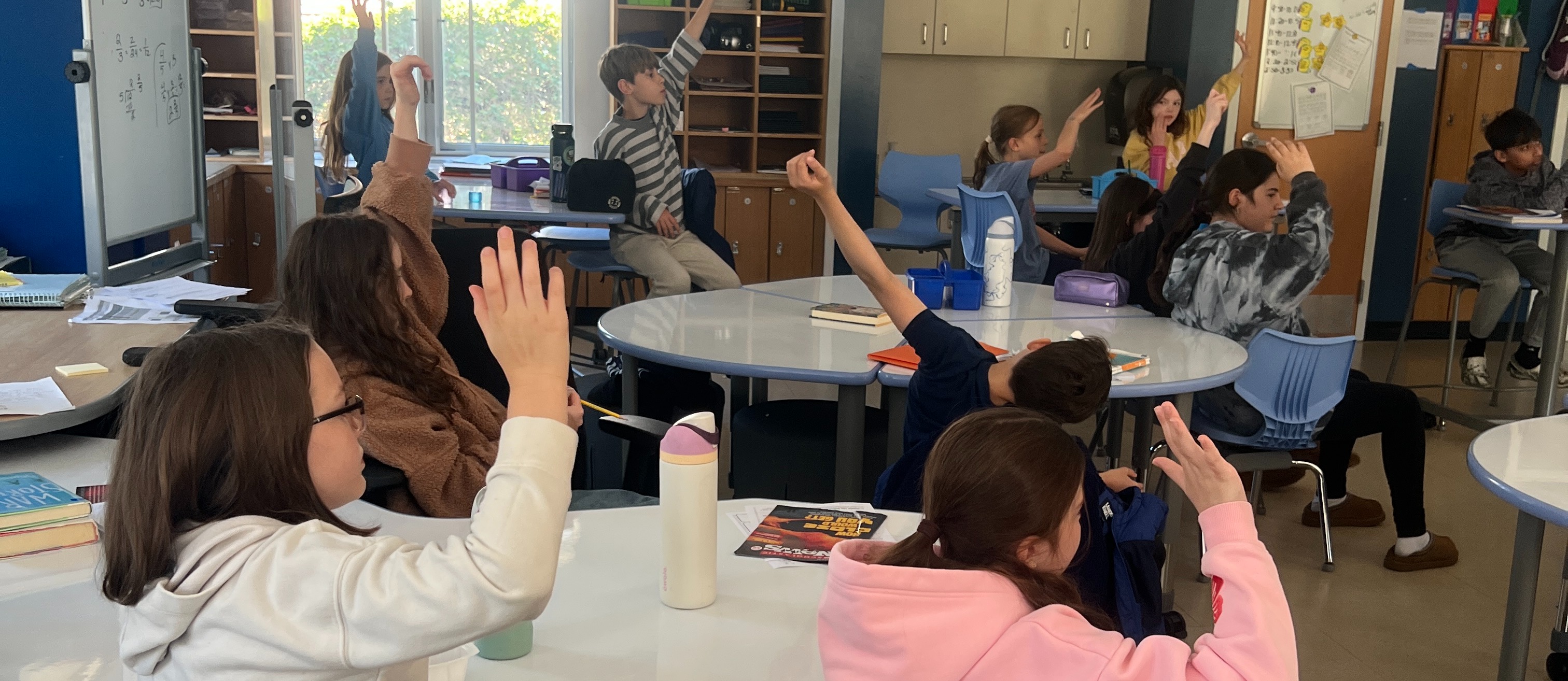 students sitting raising hands in classroom