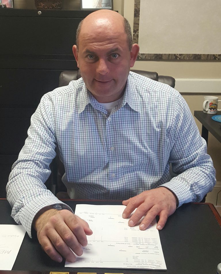 A bald man sitting at a desk with papers, deep in thought.