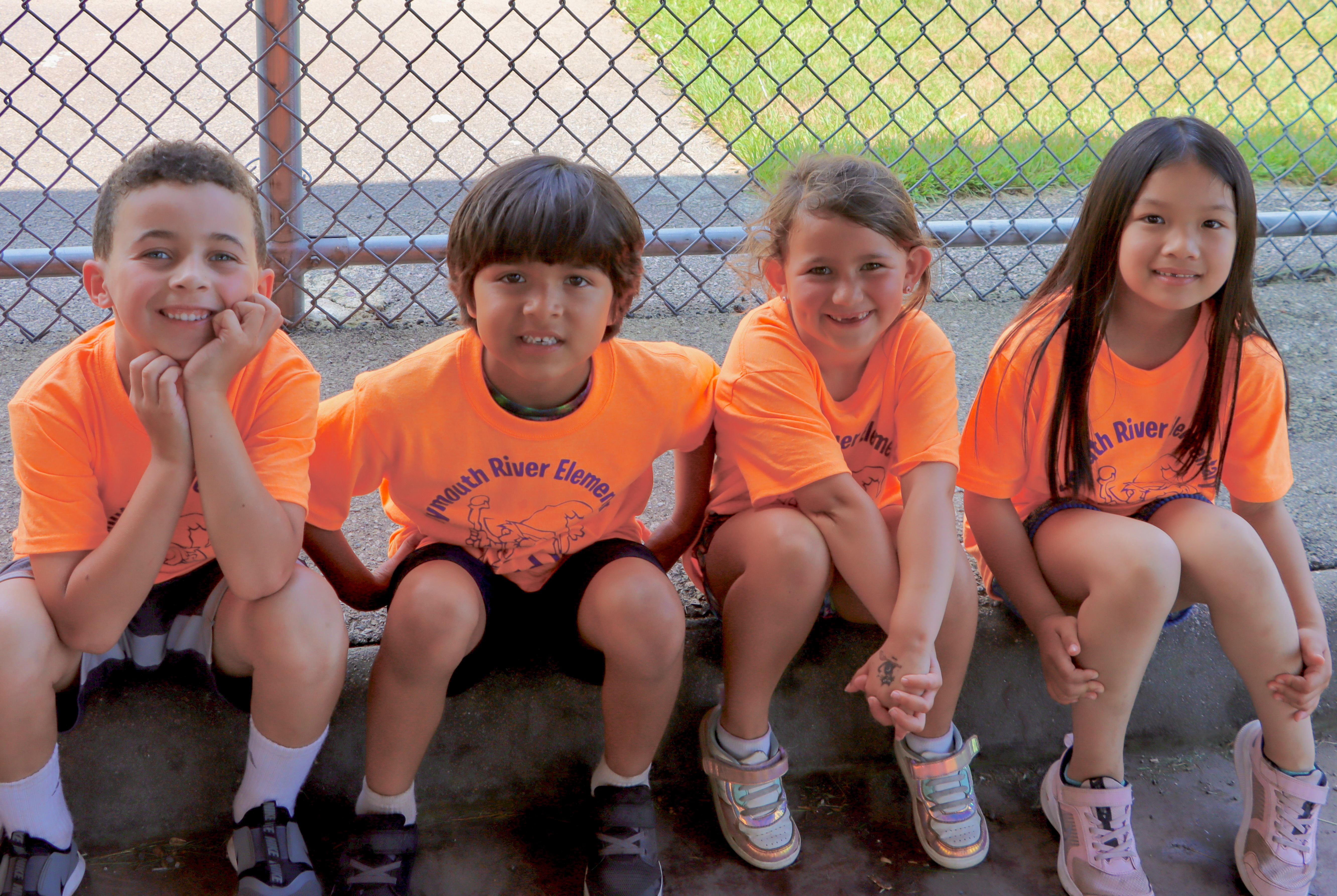 4 kindergarteners sitting together in orange shirts.