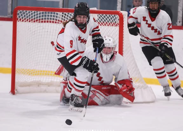 girls hockey player handling the puck up the ice. Wearing a white harborwomen jersey.