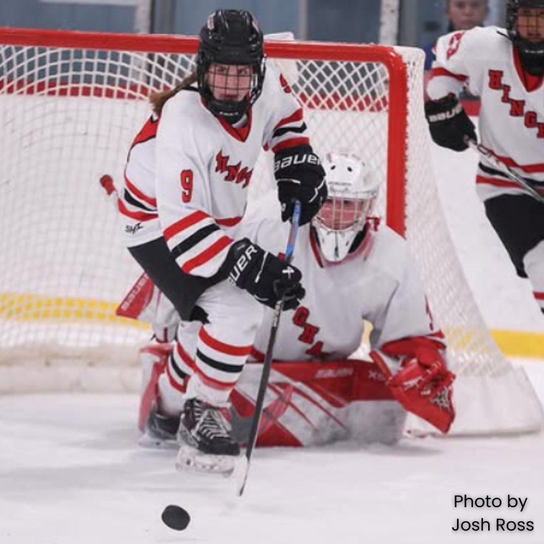 girls hockey player handling the puck up the ice. Wearing a white harborwomen jersey.