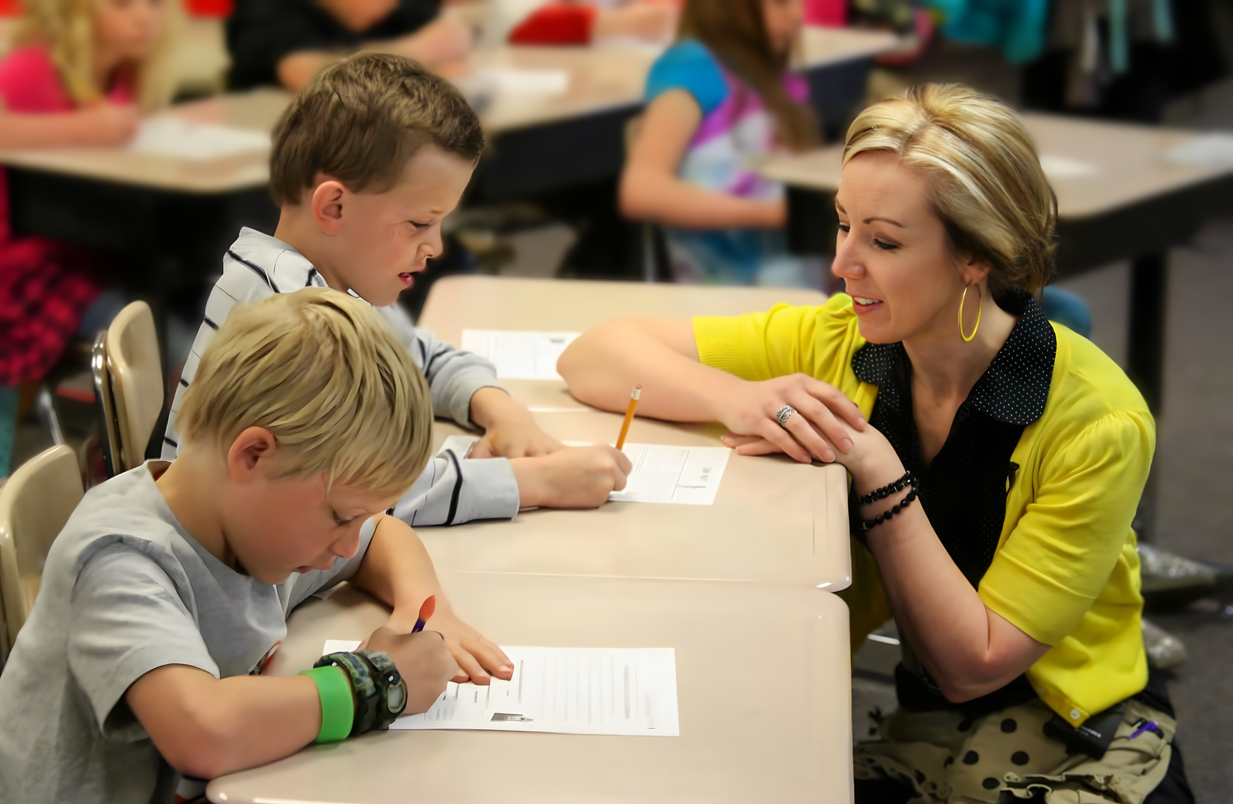 Teacher knelling in front of two students, helping with math