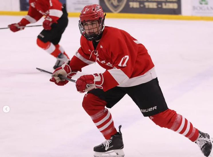 boy hingham hockey player in a red jersey skating down the ice.