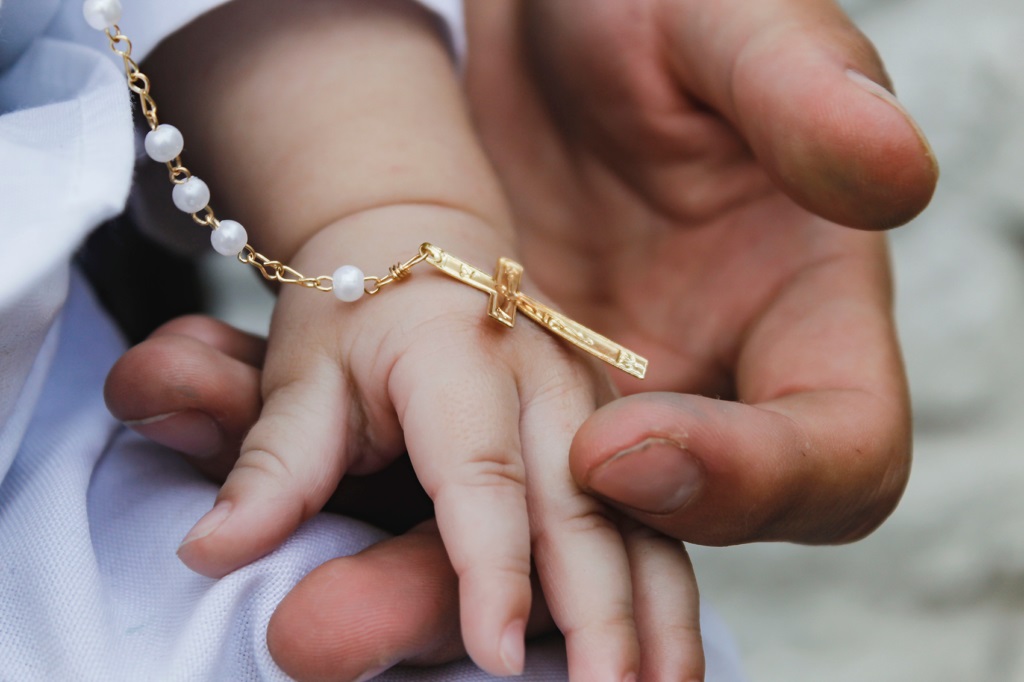 Infant and adult hands holding rosary