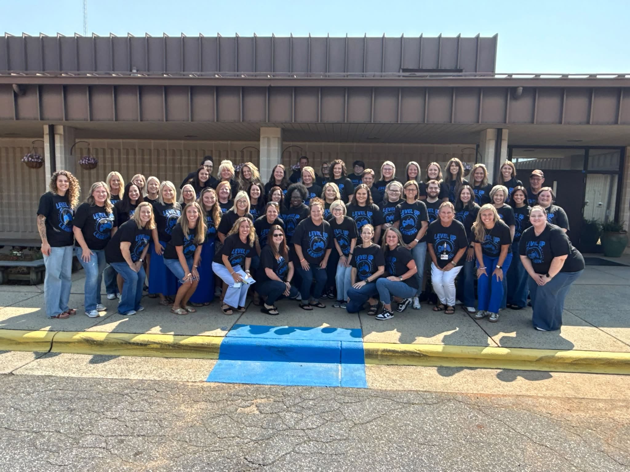 Group of people in matching shirts standing and sitting on a sidewalk in front of a building.