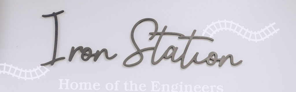 A wall sign reading "Iron Station Home of the Engineers" in script lettering, accompanied by decorative train track graphics.