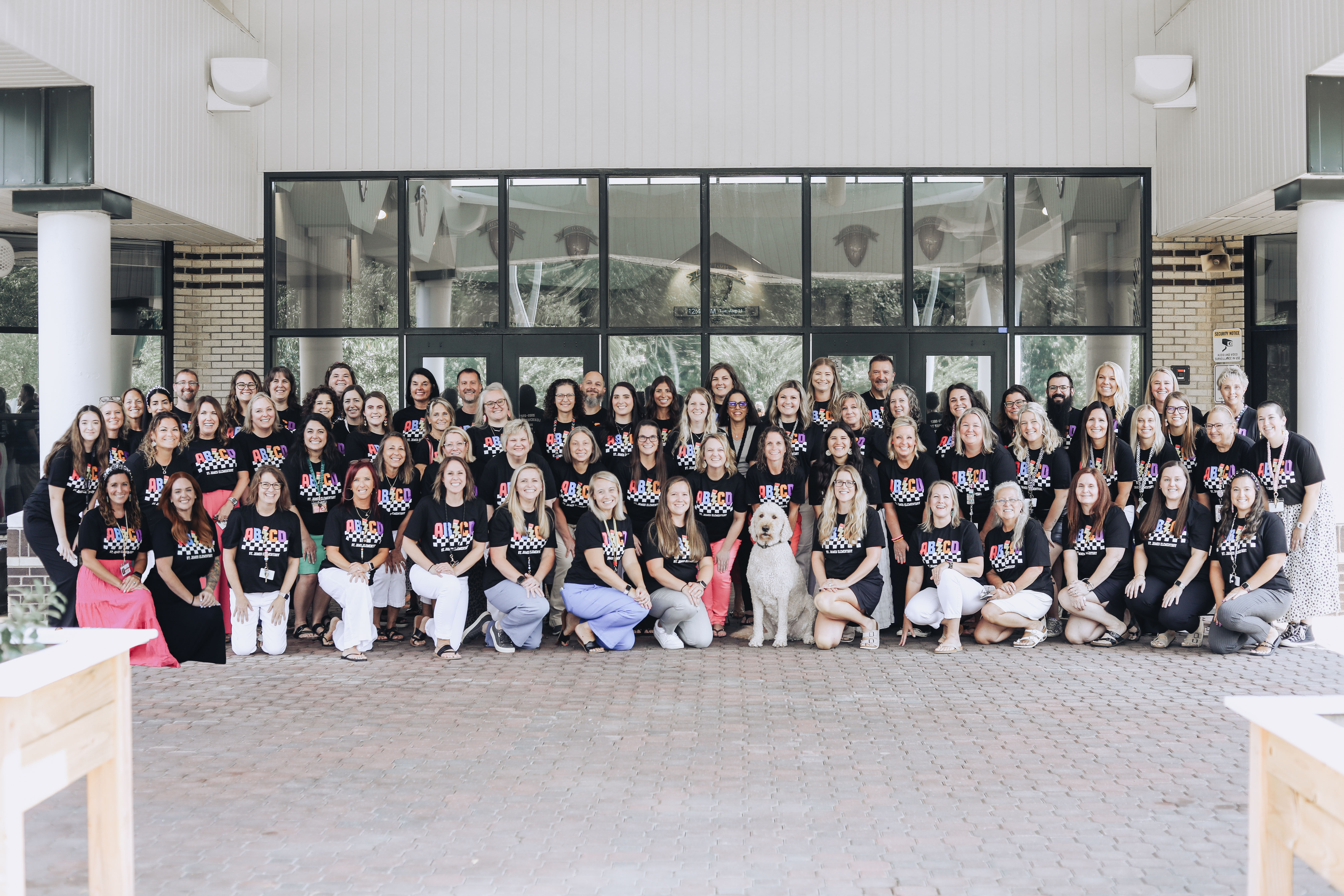 A group of people in matching shirts stand in front of a building with glass walls and pillars.